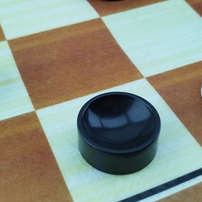 Peças de jogo de damas em preto e branco num tabuleiro quadriculado castanho e bege