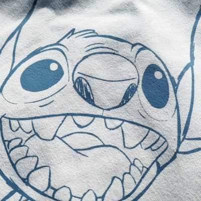 Sacola branca com estampa azul do personagem Stitch e selo colorido Brincar com Amor sobre relva