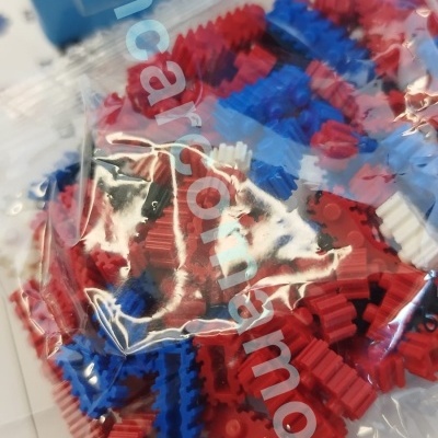 Peças de blocos de construção vermelhas, azuis, brancas e pretas em saco plástico com instruções ao fundo