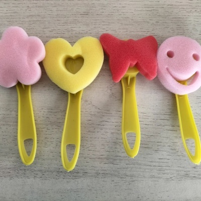 Utensílios de limpeza com esponjas coloridas e cabos amarelos em formas divertidas colocados sobre superfície de madeira.