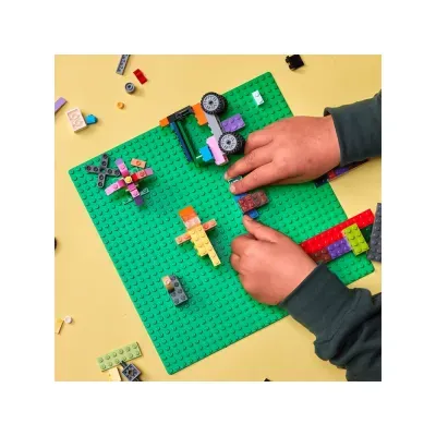 Mãos de criança a jogar com peças de LEGO coloridas sobre base verde.