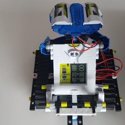 Robô de brinquedo com blocos coloridos e fios sobre superfície branca próximo a caixa