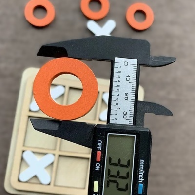 compasso digital medindo anel laranja sobre jogo da velha de madeira