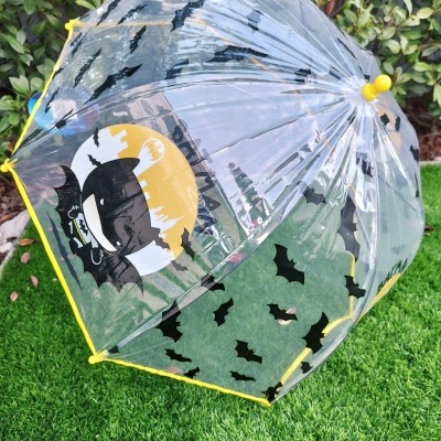 Guarda-chuva transparente com morcegos pretos e imagem de Batman, rodado em relva verde.