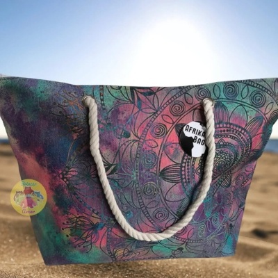 Saco de praia colorido com padrão mandala e alças de corda na areia junto ao mar