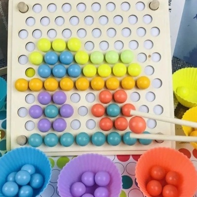 Painel de madeira com bolas coloridas e pinças, copos de silicone com bolas coloridas.