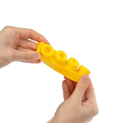 Mãos seguram bloco de construção amarelo com quatro pinos