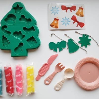 Conjunto infantil de cozinha com forma de silicone, utensílios de plástico coloridos, etiquetas verdes penduradas e prato rosa.