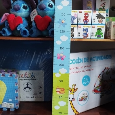 Régua de crescimento infantil azul e verde com desenhos coloridos ao lado de brinquedos em estante.