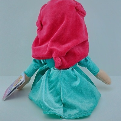 Boneca de peluche com vestido azul-turquesa e capuz rosa vista de costas