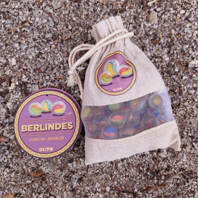 Saco de pano com berlindes coloridos e etiqueta roxa e amarela sobre terra com pedras