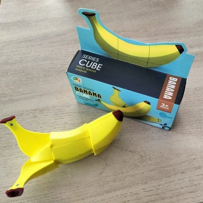 Brinquedo cubo mágico banana amarela com caixa azul sobre mesa de madeira clara