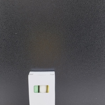 Caixa branca com três objetos coloridos visíveis numa janela, sobre madeira e fundo preto.