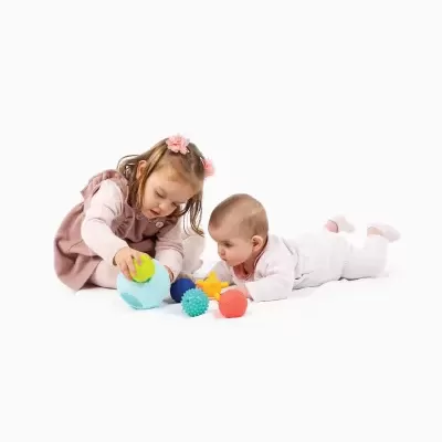 Duas crianças brincando no chão com brinquedos coloridos de várias formas e texturas