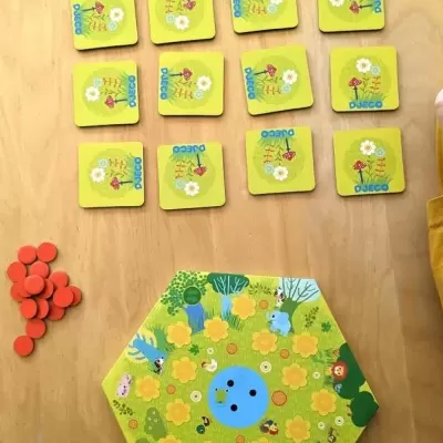 Jogo de tabuleiro infantil com peças amarelas e fichas vermelhas sobre madeira