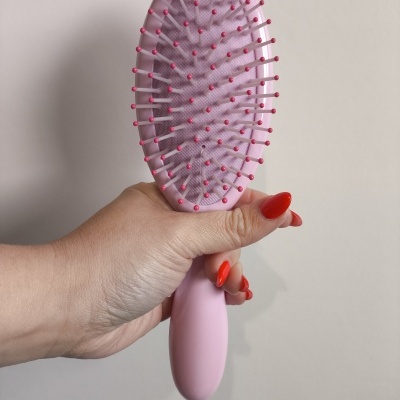 Escova de cabelo oval rosa com cerdas cor-de-rosa segurada por mão