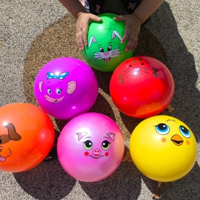 Balões coloridos com desenhos de rostos de animais e mãos de criança a segurar um balão verde.