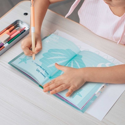 Caderno azul com desenhos marinhos e criança a escrever numa mesa branca