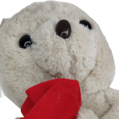 Peluche bege com nariz castanho e olhos pretos segurando objeto vermelho