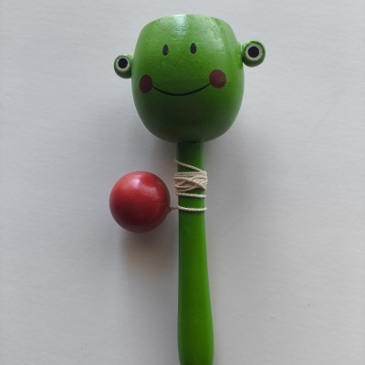 Jogo de madeira verde com rosto sorridente e bola vermelha presa por cordel