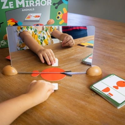 Jogo educativo com espelho e peças coloridas sobre mesa de madeira