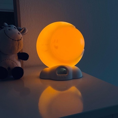 Lâmpada de mesa redonda amarela com base cinzenta e ecrã digital ao lado de peluche de vaca