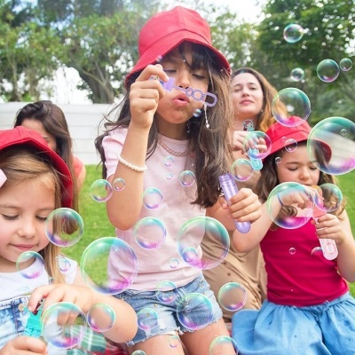 Crianças a brincar com bolhas de sabão ao ar livre com chapéus vermelhos