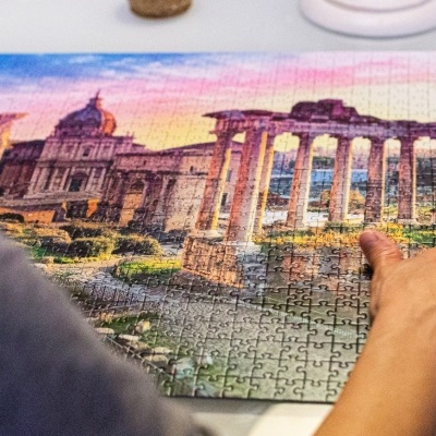 Pessoa montando puzzle com cenário histórico de ruínas e edifícios coloridos.