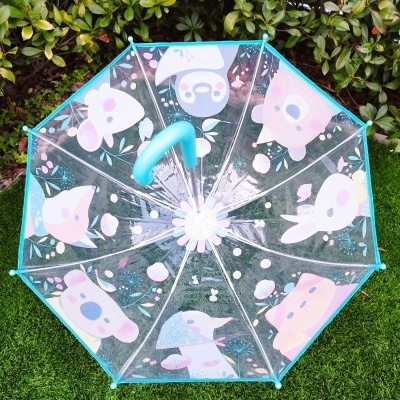 Guarda-chuva transparente com desenhos coloridos de animais e flores, cabo azul, sobre relva verde