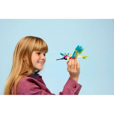 Menina loira a sorrir segura um brinquedo de construção colorido em forma de pássaro