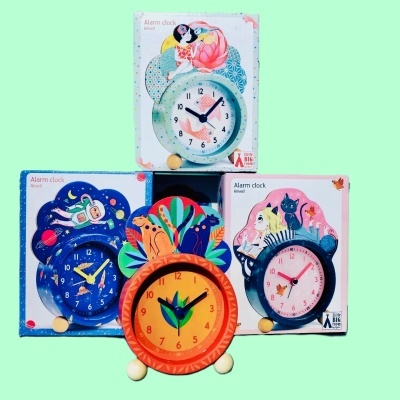 Quatro relógios despertadores coloridos com design decorativo e embalagens com texto 'Alarm clock'