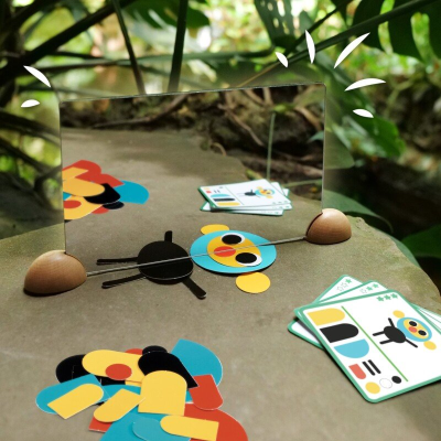 Espelho com suportes de madeira e peças coloridas ao lado, em ambiente exterior.