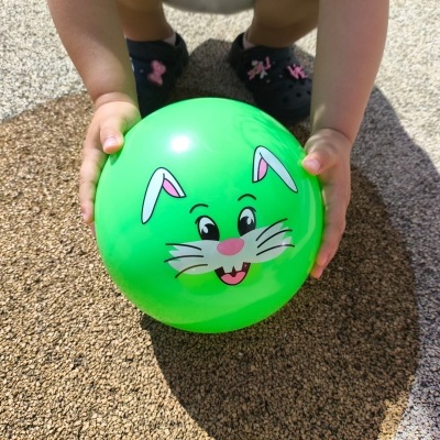 Bola verde com rosto de coelho segurada por criança em chão texturizado