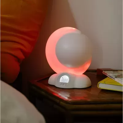 Lâmpada de mesa branca com luz vermelha e visor digital em mesa junto a almofada e livros