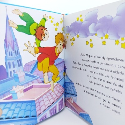 Livro infantil ilustrado aberto com crianças voando sobre telhados e texto em português.