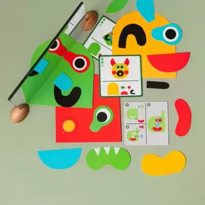 Peça de jogo infantil colorida com espelho e cartas sobre fundo verde