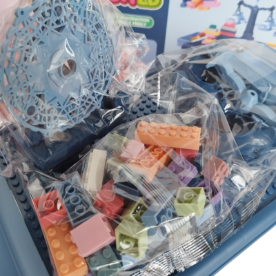 Peças de construção coloridas em sacos transparentes sobre base azul clara com caixa colorida ao fundo