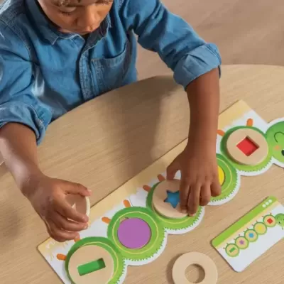 Brinquedo educativo de madeira com peças geométricas coloridas e criança a brincar sentado