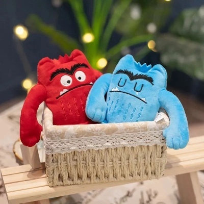 Bonecos de peluche vermelho e azul com expressão facial numa cesta de tecido creme