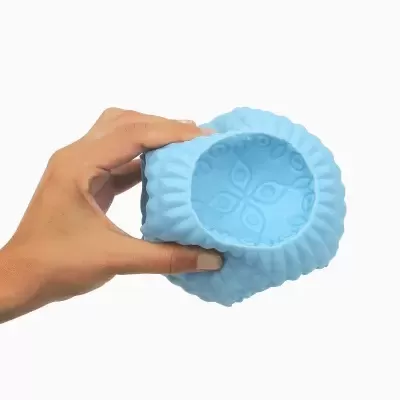 Dispositivo massageador azul de silicone com padrão floral segurado por mão