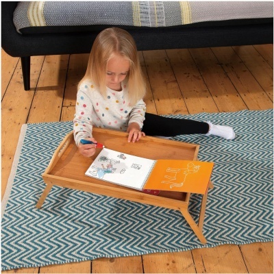 Criança a desenhar numa mesa-baixa de madeira portátil sobre tapete azul e branco zig-zag