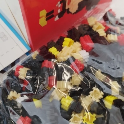 Pequenos blocos plásticos coloridos em sacos transparentes com caixa vermelha ilustrada ao fundo