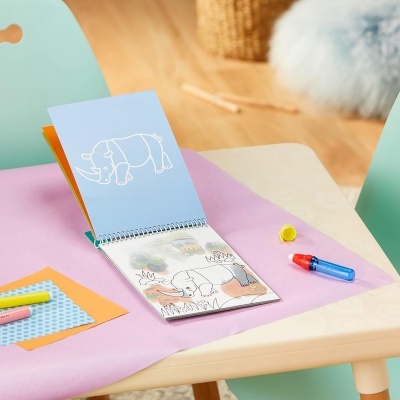 Caderno de desenho aberto com ilustração de rinoceronte sobre mesa com papel rosa e canetas coloridas