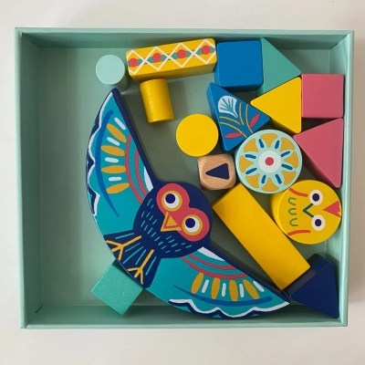 Blocos de construção coloridos em madeira com formas geométricas e coruja azul numa caixa azul clara.