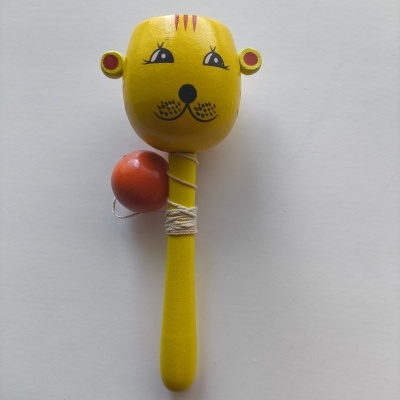 Maraca de madeira amarela com desenho de animal e bola laranja presa ao cabo.