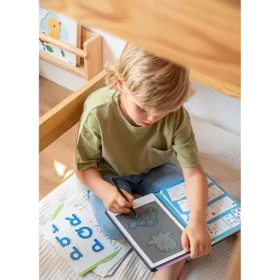 Criança a desenhar num tablet sentado numa cama de madeira clara