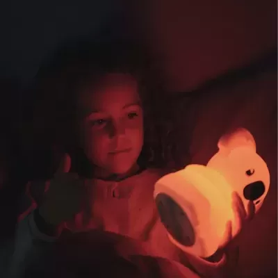 Criança a segurar uma luz noturna em forma de urso iluminada em ambiente escuro