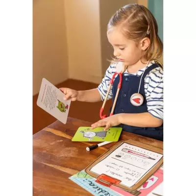 Criança com estetoscópio de brinquedo a brincar com cartas educativas numa mesa de madeira