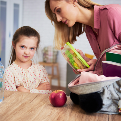 Mulher a colocar lancheira na mochila ao lado de maçã e garrafa de água em ambiente interior