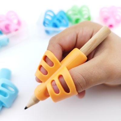 Mão a segurar lápis com pega ergonómica laranja e pegas coloridas ao fundo